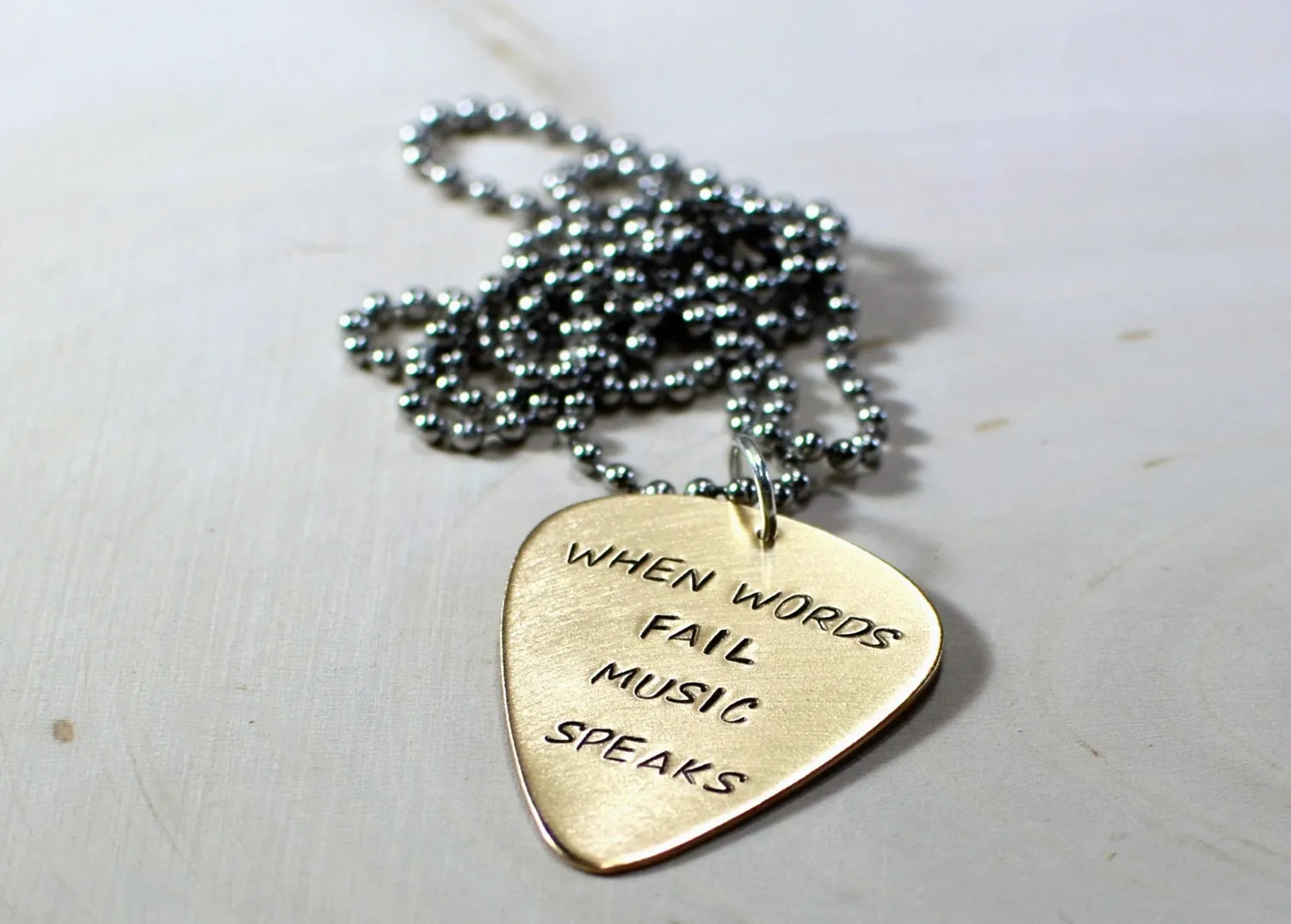 Bronze guitar pick necklace stamped with When words fail music speaks