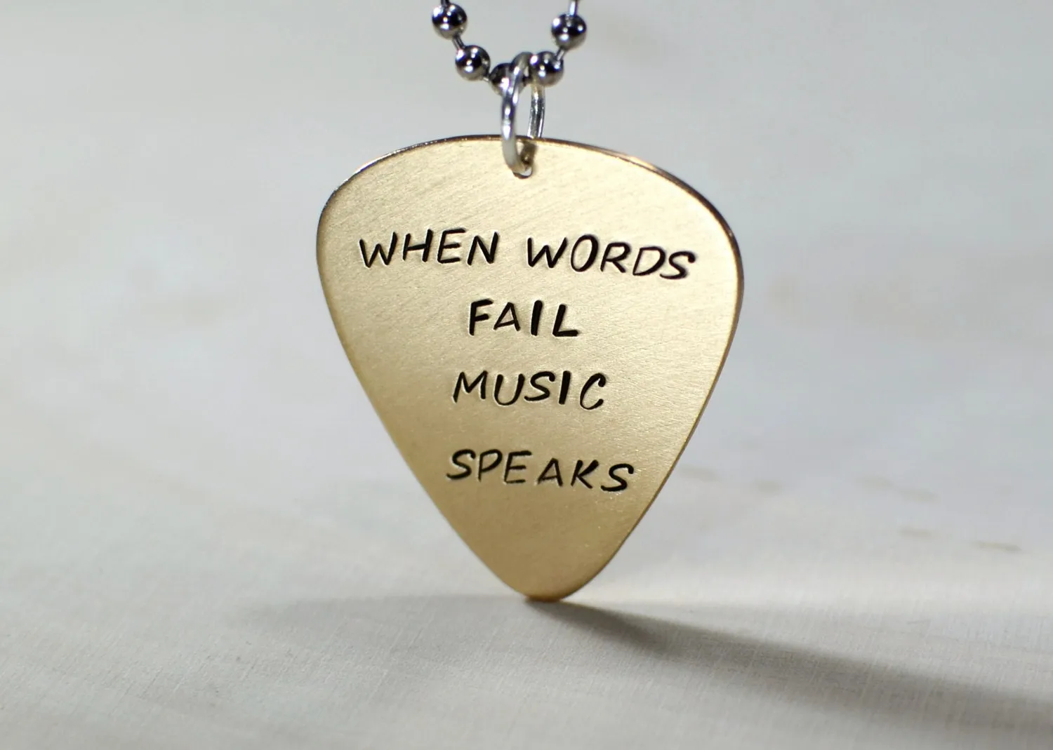 Bronze guitar pick necklace stamped with When words fail music speaks